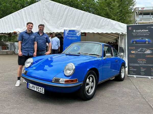 Der Geschäftsführer Roland Heidl und ein Angestellter stehen bei einer Veranstaltung neben dem blauen Porsche 911